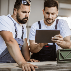 Two men working in a carpentry studio, holding a tablet with VIVED Learning Carpentry Course